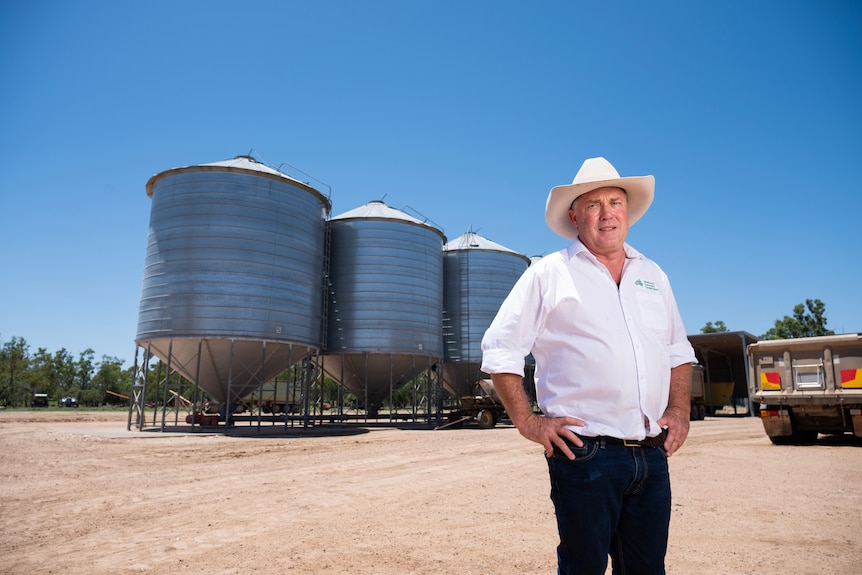 A man in a hat stands in front of silos.
