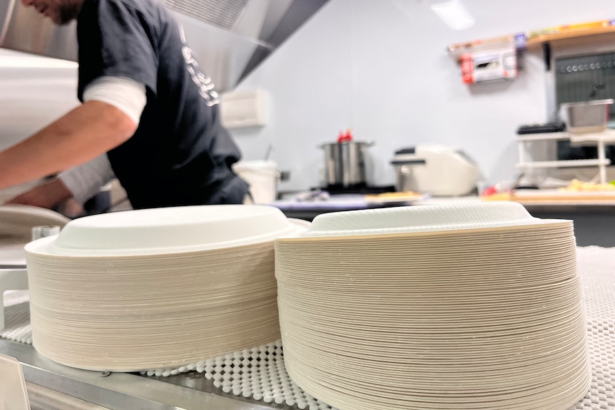 Two stacks of paper plates on a bench in an industrial kitchen.