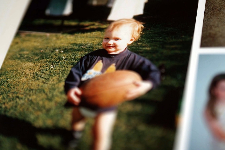 A photo in a page of a photo album of a toddler holding a football, it is large in the young boy's hands.