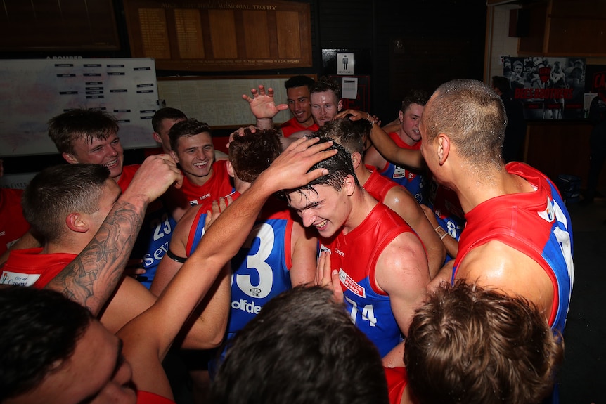 Members of an AFL team congratulate each other. One is touching a player on the head.