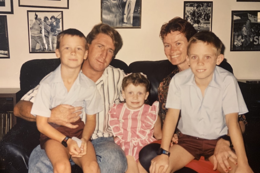 Erin with her mum, dad and brothers as young kids, sitting on a couch with two boys in parents' laps and girl in the middle.