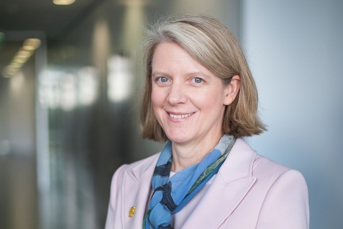 A woman with short blonde hair and business attire smiles at the camera.