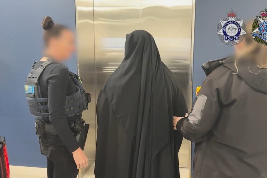 A woman in black Islamic garb is flanked by two uniformed police officers.