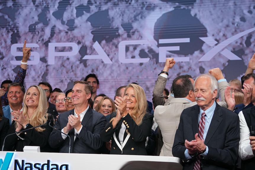 A group of people clap and raise their arms with SpaceX branding behind them.