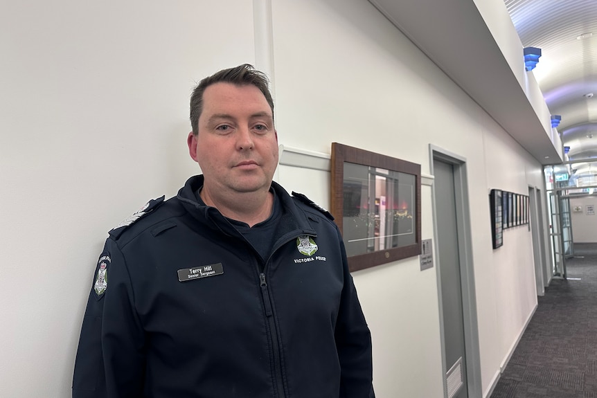 Police officer man looking seriously into camera, in hall way within the Stawell police building, frames on walls.