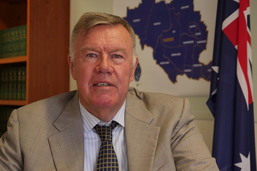 A man sites in an office in front of an Australian flag.