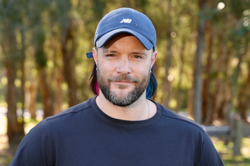 A man with a beard, wearing a blue cap and sweatshirt, smiling.