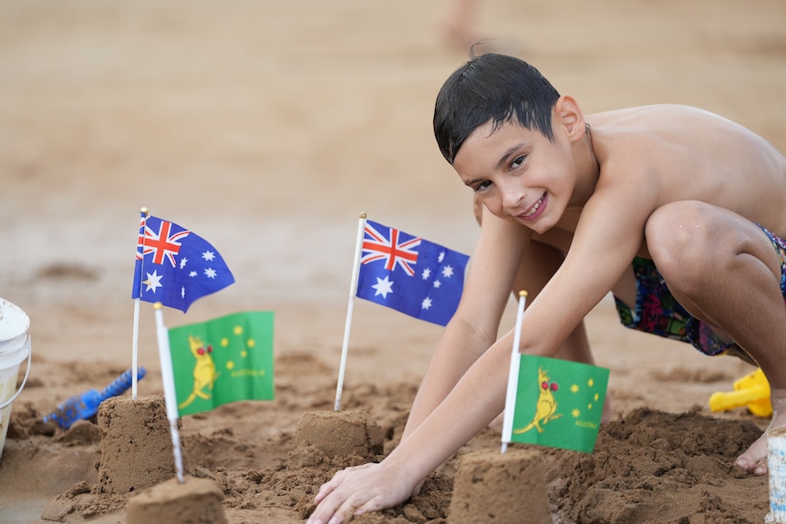 Boy makes sand castles with Australian and boxing kangaroo flags sticking out of them