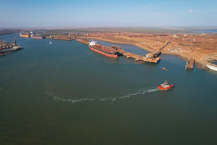 A small tugboat leaves a white trail in its wake with a bulk carrier behind it in the harbour.