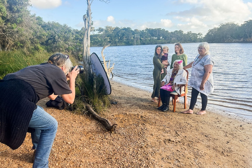 A person taking a photo with a group of five females in front of the water.