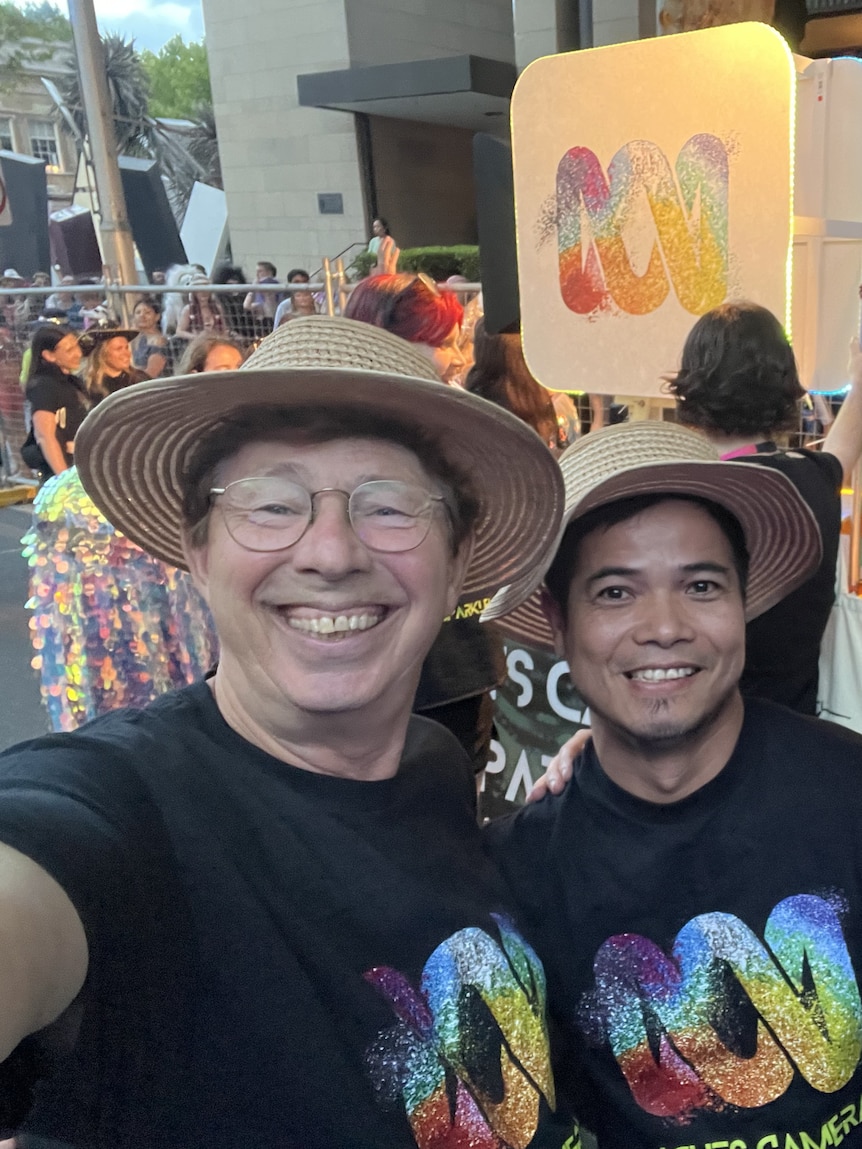Jerry and Tuan grinning at a parade, surrounded by confetti, wearing ABC shirts in rainbow