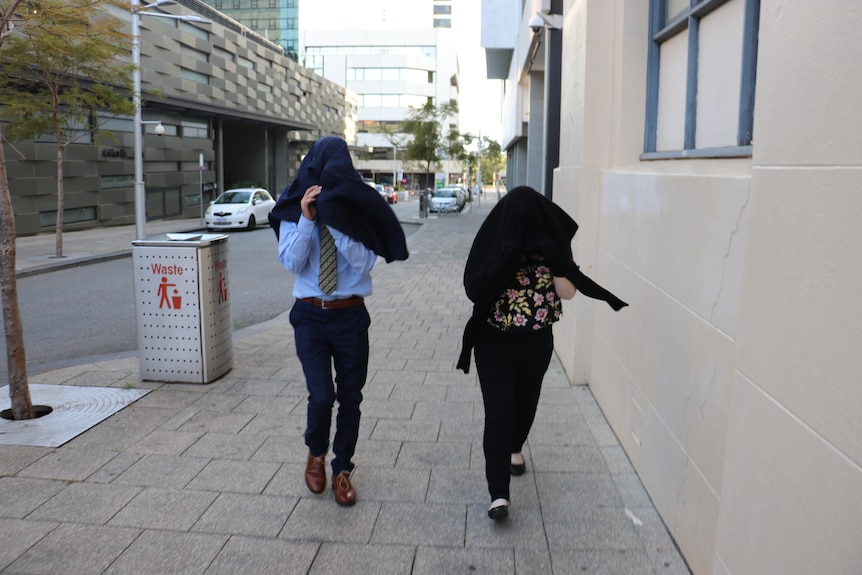 A man and woman walking down the street, covering their heads with jackets