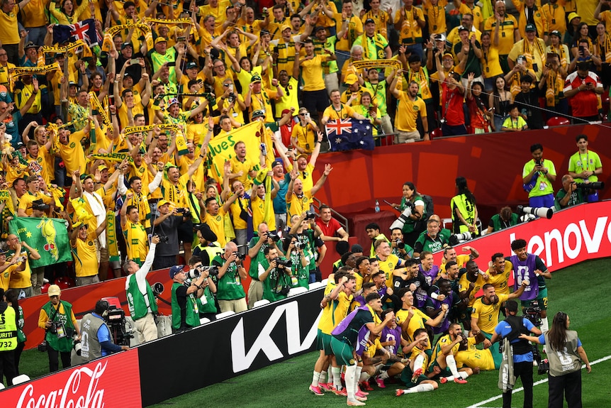 Socceroos players pose for a photo in front of a sea of supporters dressed in yellow.
