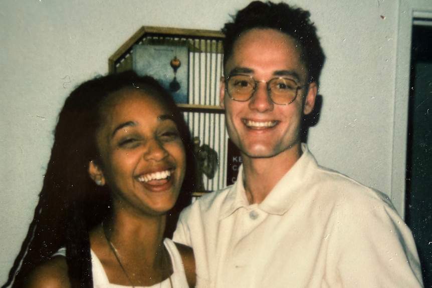 A young dark-skinned woman with long hair stands next to a tall young white man. They are both smiling.