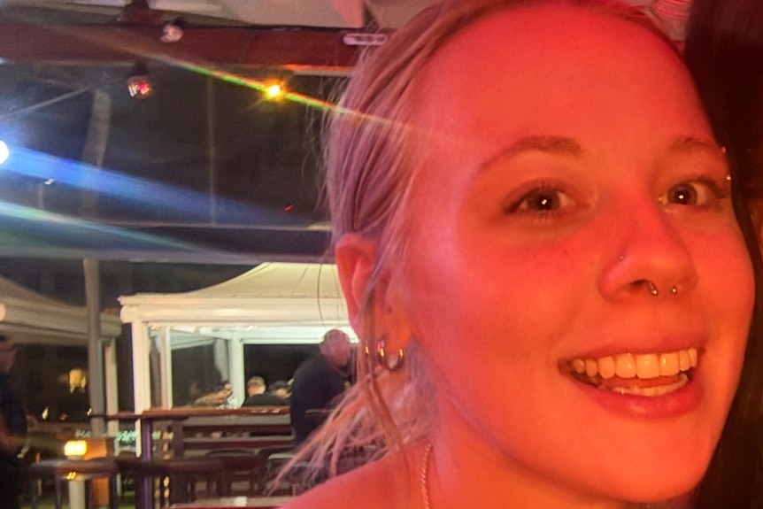A woman smiling in a selfie with red light on her face under a marquee