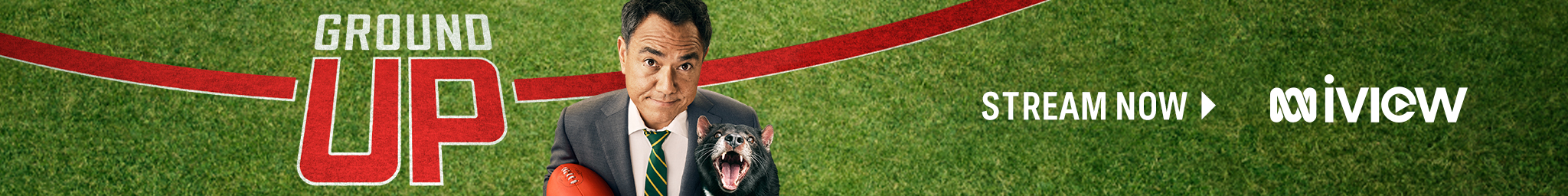 Sam holds an AFL football in one hand and a Tassie Devil in the other as he stands on a sports pitch