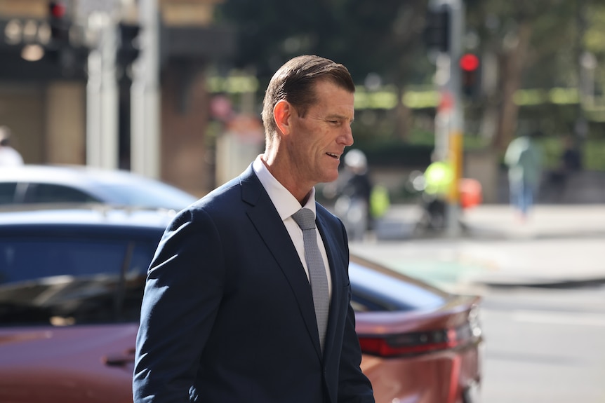 Ben Roberts-Smith entering Downing Centre Sydney in a suit and tie, a bus and car behind him.