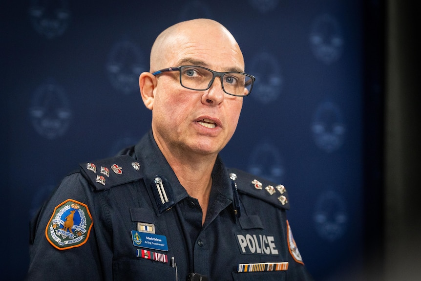 A uniformed police officer wearing reading glasses as he addresses the room.