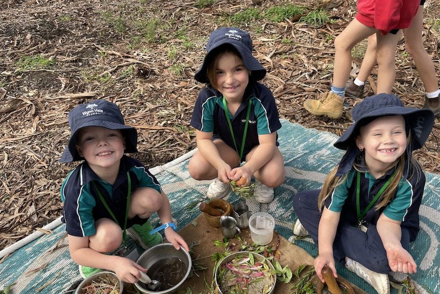 Three kids in school uniform play with leaves in kitchen pans