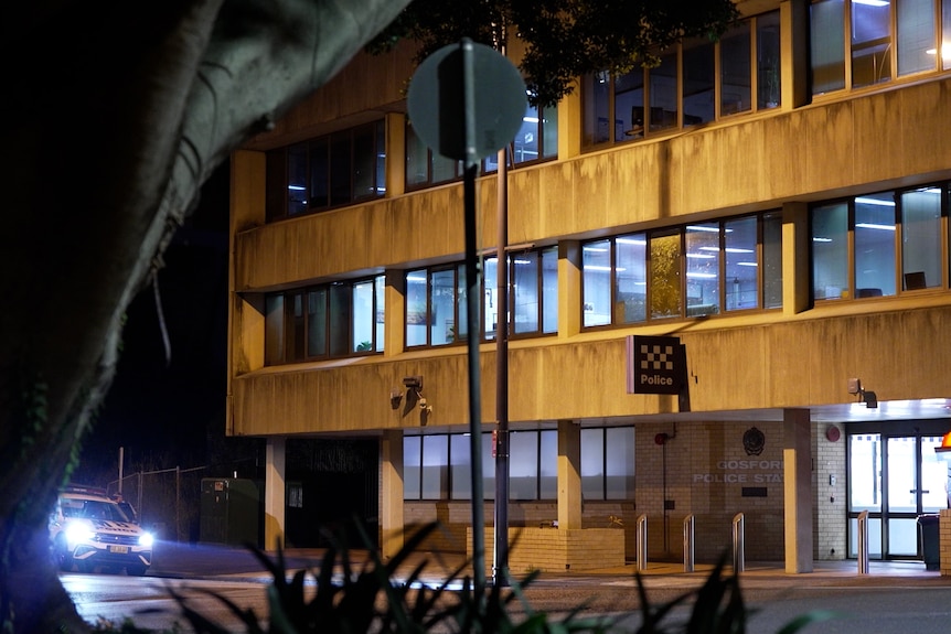 A concrete multi-story building with lights on inside and a Police sign at night.