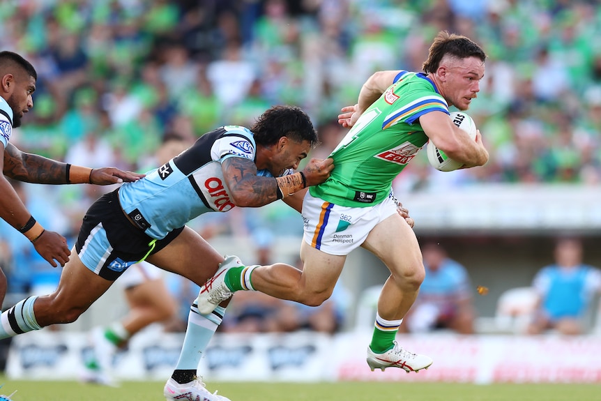 Tom Starling holds the ball and runs as another rugby league player grabs his jersey from behind.