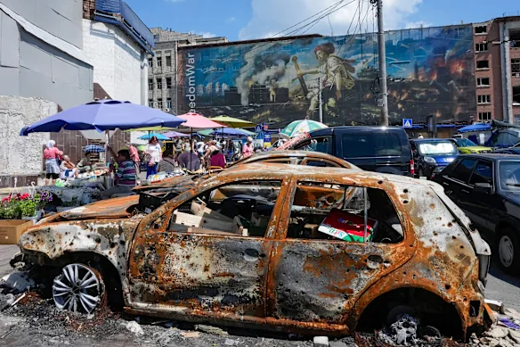 People buy food at an improvised outdoor market in Kyiv this month, amid cars and building damaged by Russian attacks.
