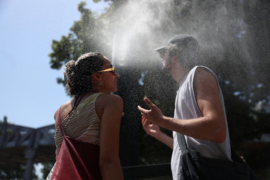 Two persons use a water mister on a street in Paris.