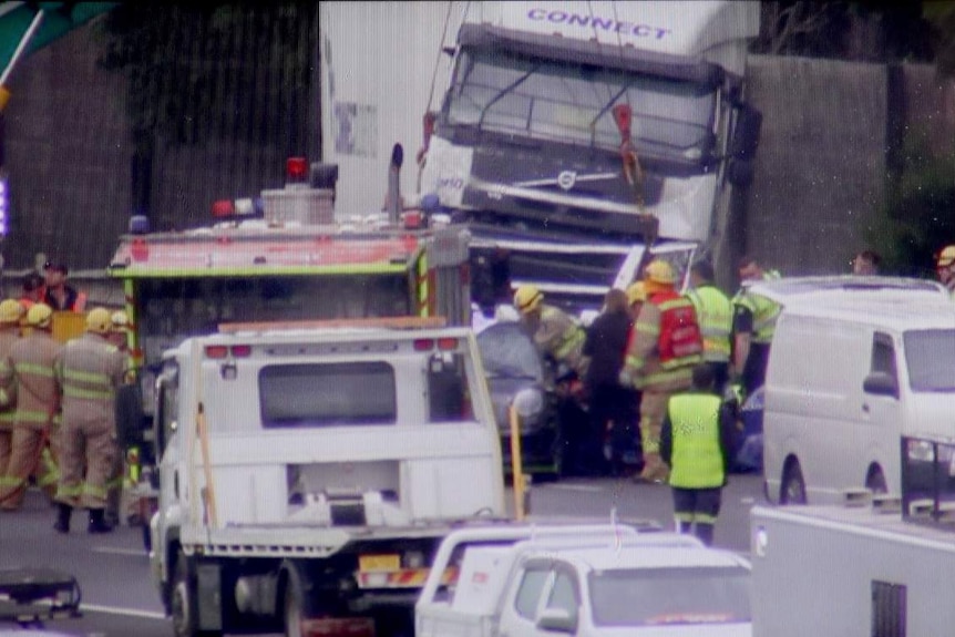 A truck and car can be seen mangled, while a number of firefighters stand around the outside.