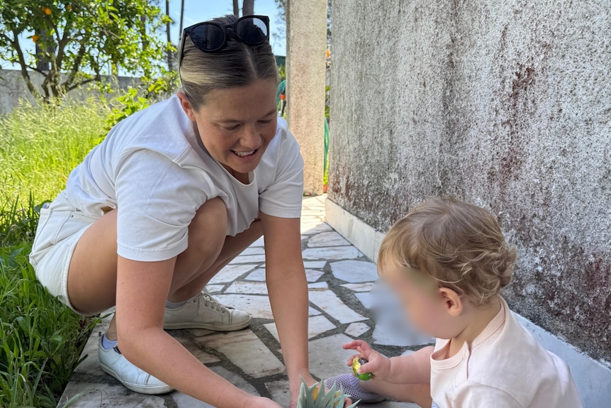 A blonde woman in a white shirt playing with a baby.