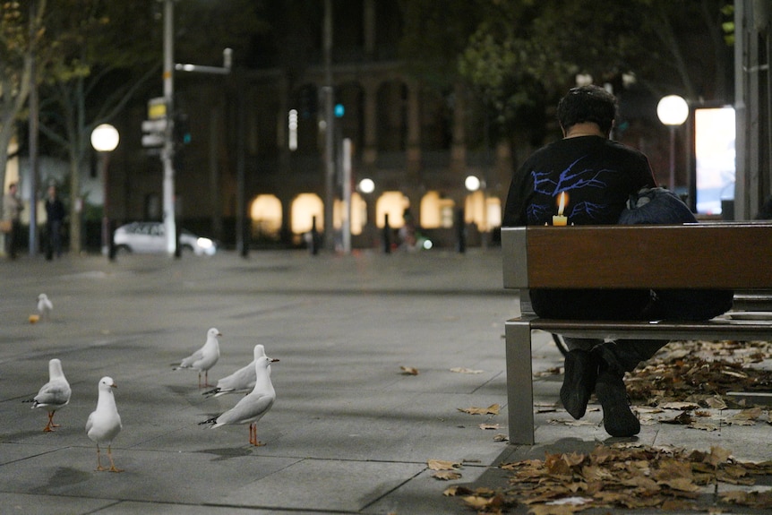 A man sitting outside on a park bench at night.