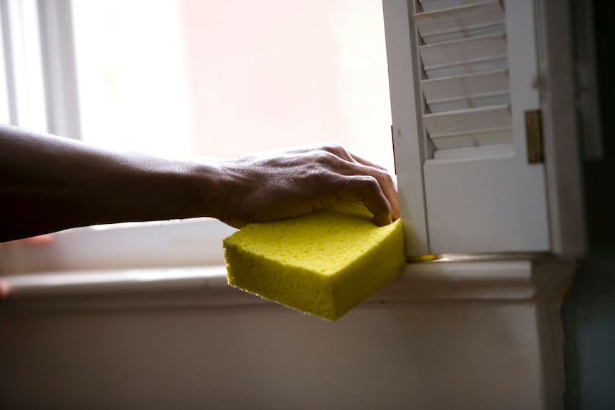 A gloved hand wipes a window sill.