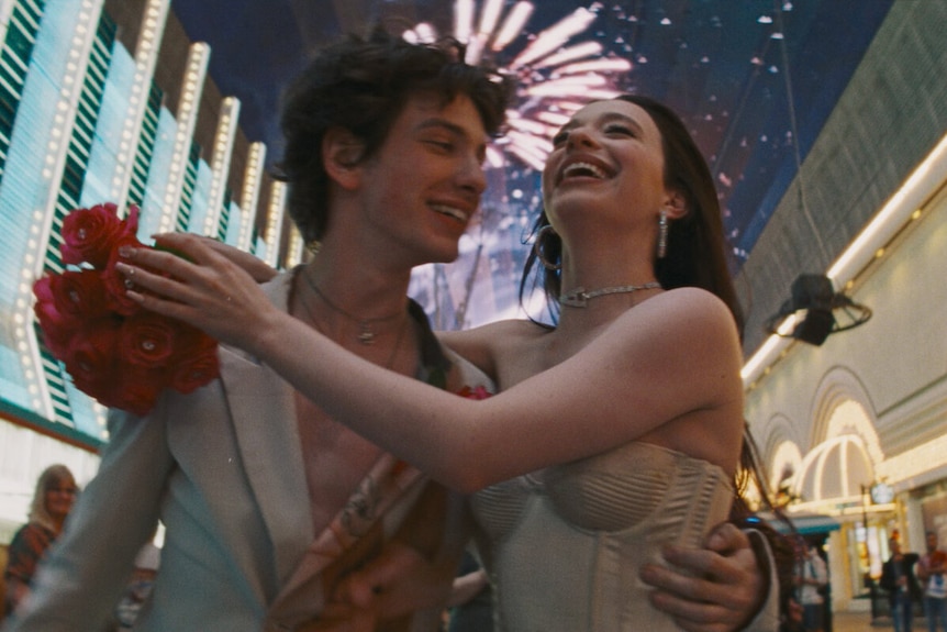 A young man and women smiling, staring at each other in wedding attire.