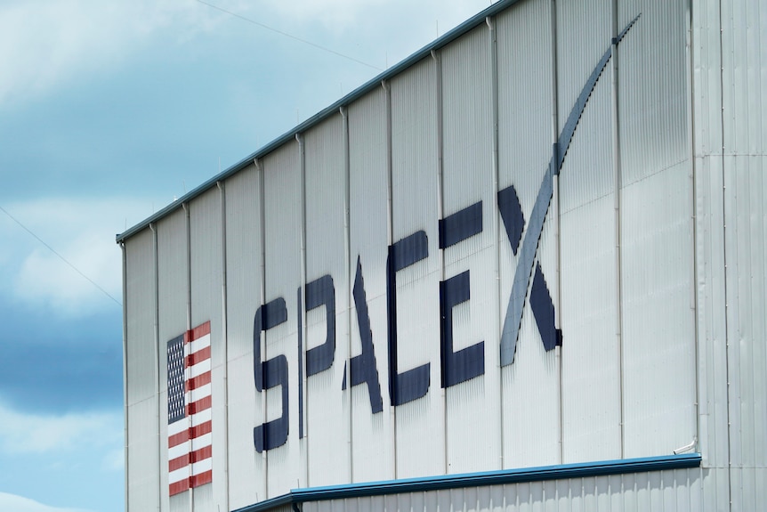 a sign with large letters on the side of a warehouse stating Space X and an american flag