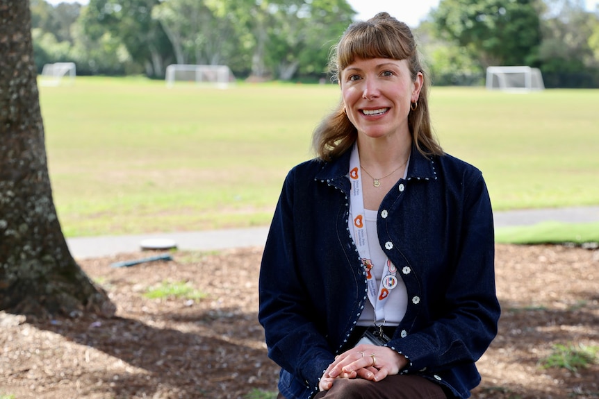 A woman in a dark blue top sits under a tree on a seat