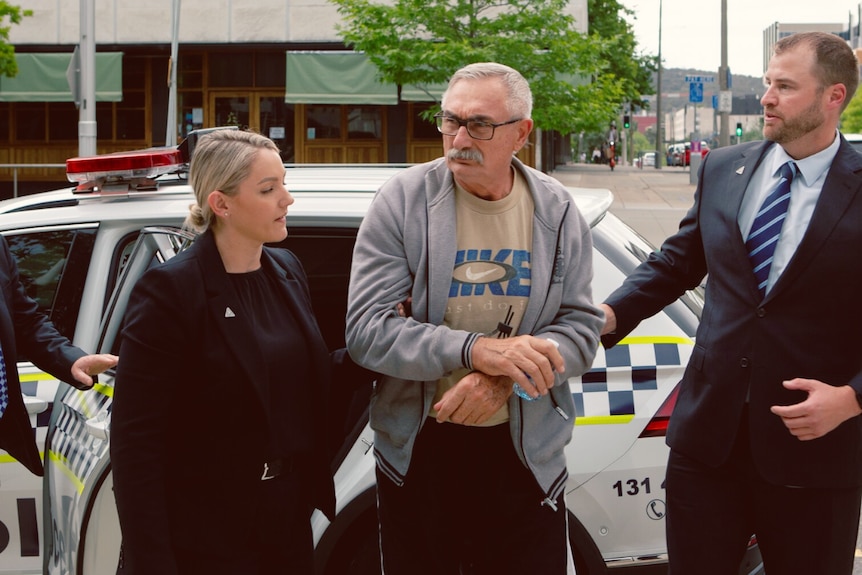 A man being escorted out of a police vehicle. 