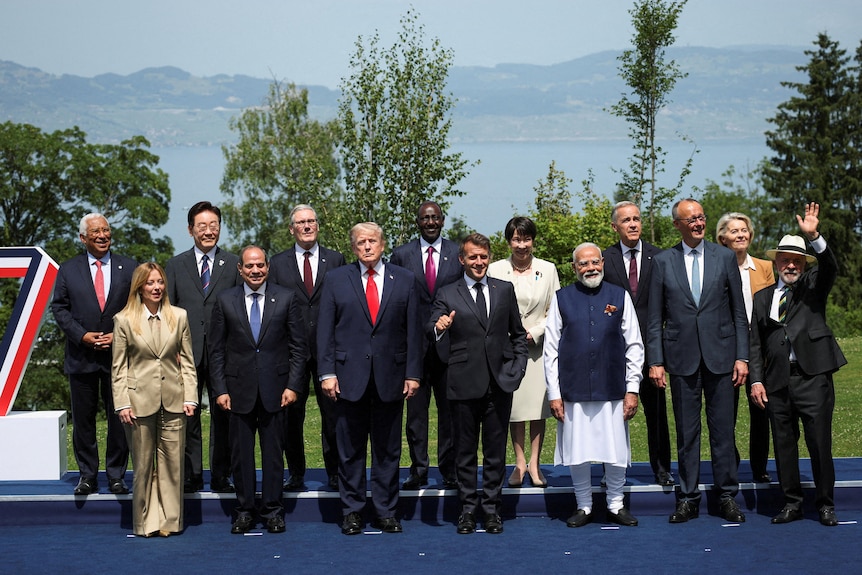 A group of world leaders in formal clothing pose for a group photo in front of a lake