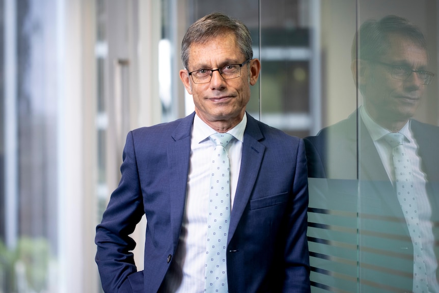 Man in suit leaning on glass window and a slight smile