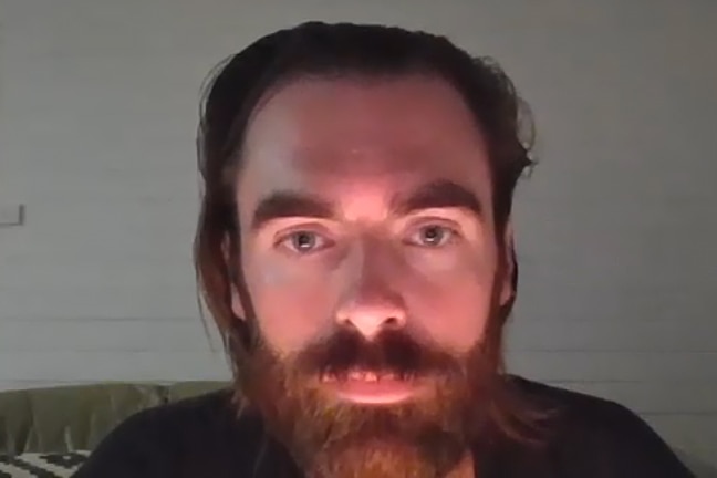 A close-up shot of a man with long brown hair and a beard, appearing on a video call for a podcast.