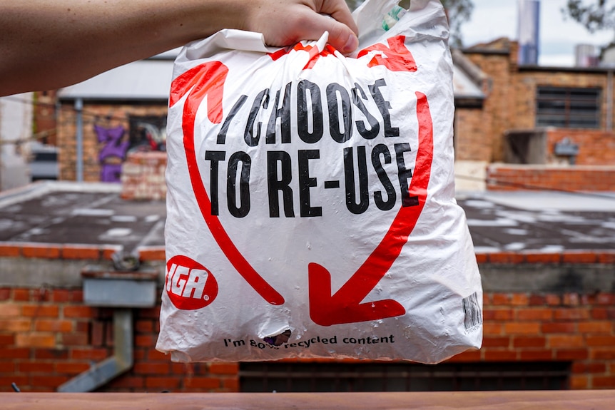 A person holds a plastic bag with the slogan 'I choose to re-use' on the front.