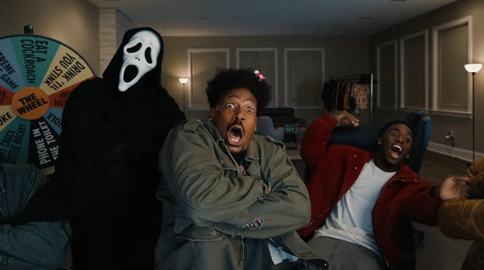 Person in horror mask scaring two men in house with colorful challenge wheel.