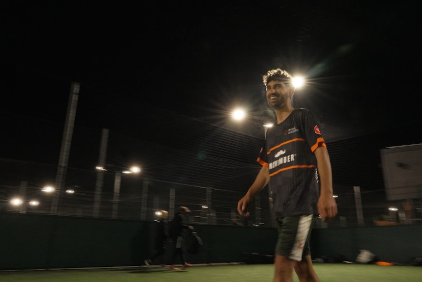A man in black on a soccer field at night.