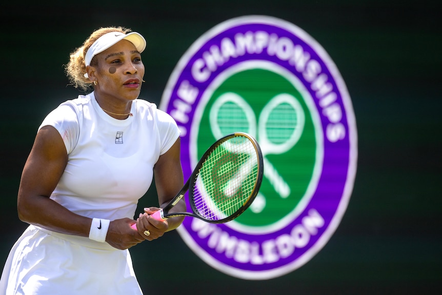 Serena Williams holds her tennis racquet in front of a the Wimbledon logo.
