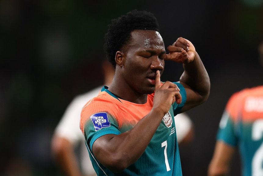 Soccerooss player Nestory Irankunda has a finger on his lips shushing and other hand pointed to his head