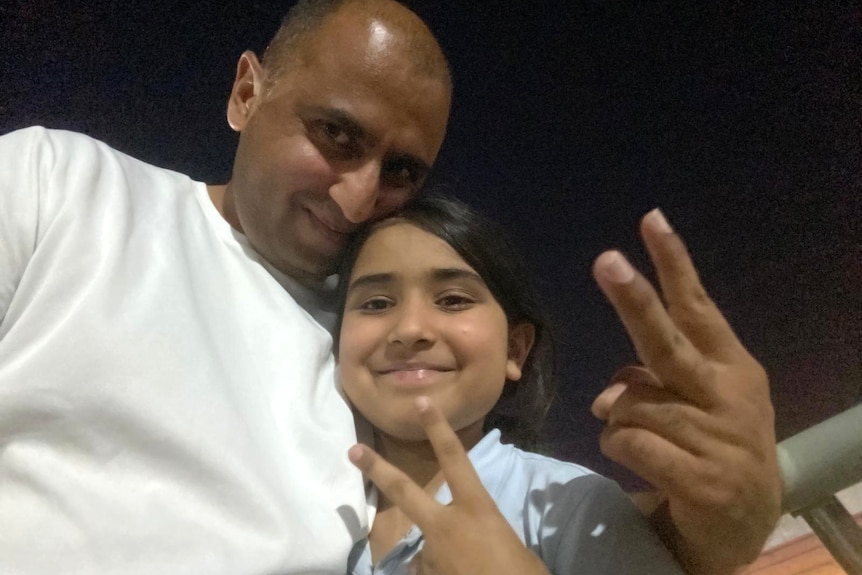 Selfie of a man hugging his young daughter and forming finger signs.