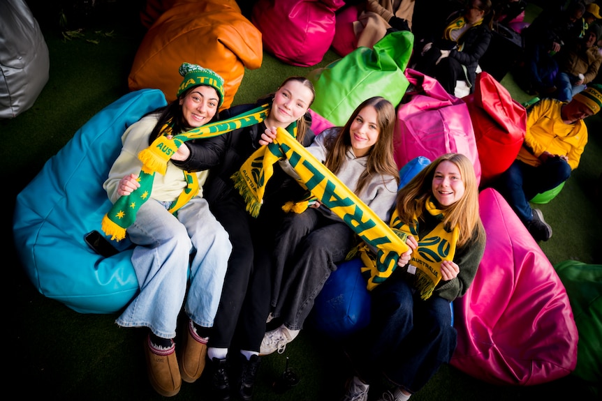 Four smiling young women sit on bean bags and show off colourful scarfs