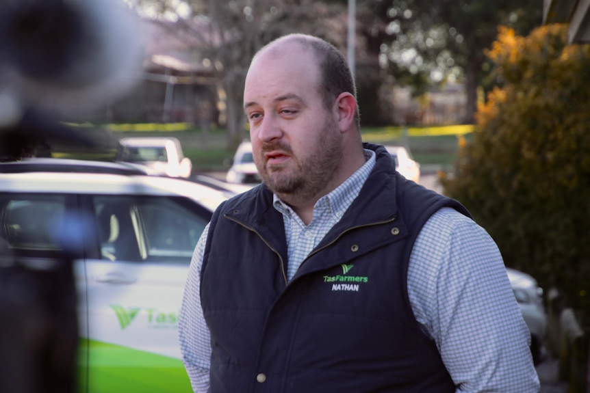 A man in a TasFarmers vest stands before TV cameras.