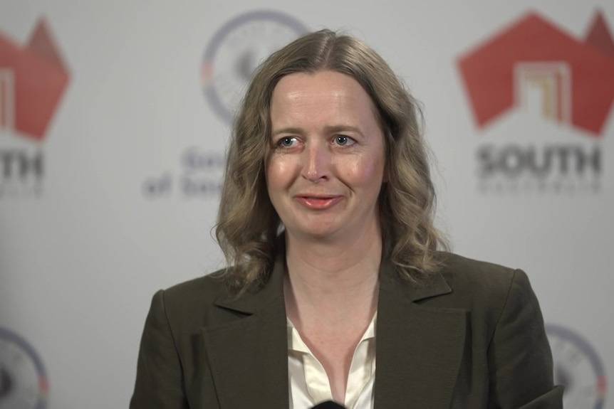 Emily bourke stands in front of a microphone and the SA logo