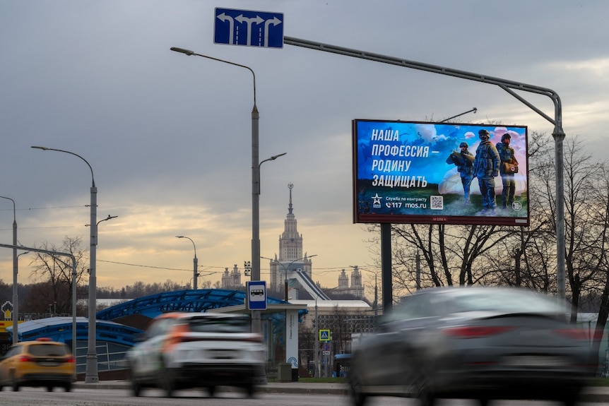Cars drive near a billboard that has a picture of soldiers on it.