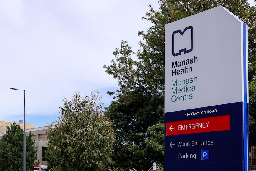 Hospital sign stating "Monash Health, Monash Medical Centre". Buildings in the background.
