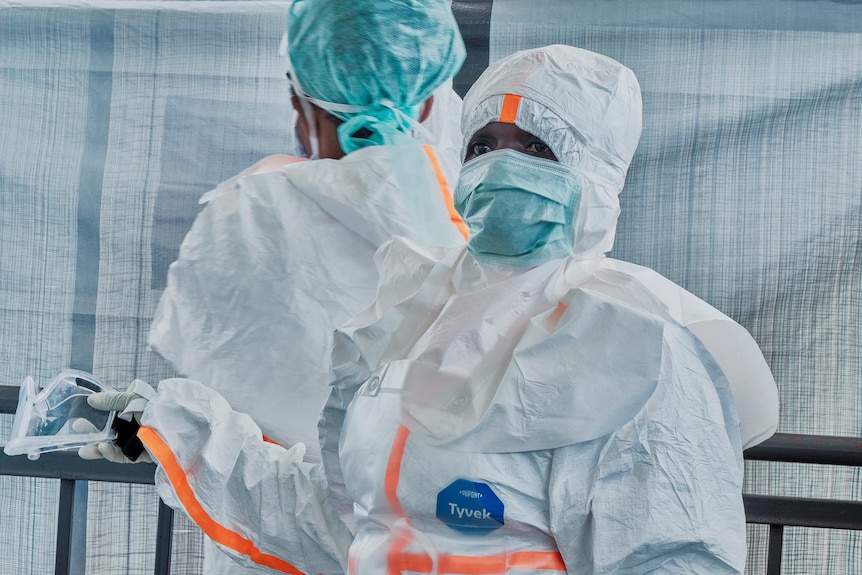 A person wearing full-body and face PPE including a face mask standing in a medical tent.